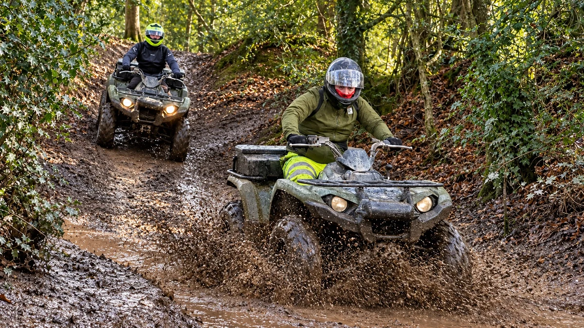 Two helmeted quad riders following a muddy woodland trail